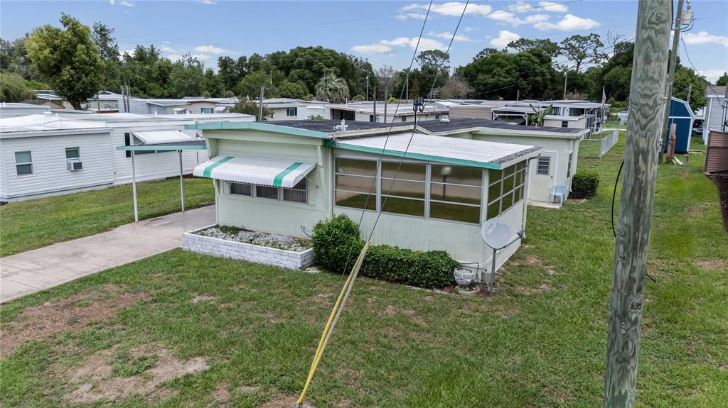 An exterior view of a light green mobile home with a screened-in porch and carport — 5238 BETMAR DRIVE, ZEPHYRHILLS, FL