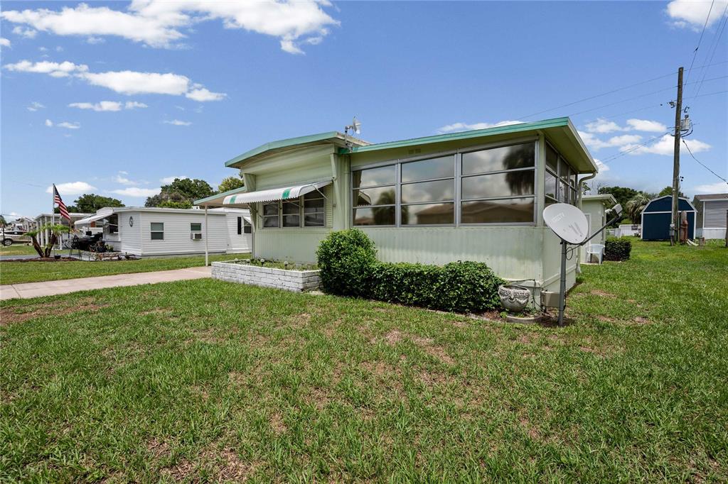 A light green mobile home with a screened-in porch sits on a grassy lot — 5238 BETMAR DRIVE, ZEPHYRHILLS, FL