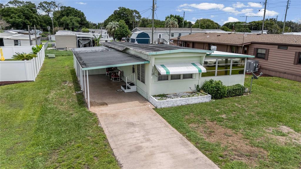 An exterior view of a light green mobile home with a carport and attached sunroom — 5238 BETMAR DRIVE, ZEPHYRHILLS, FL