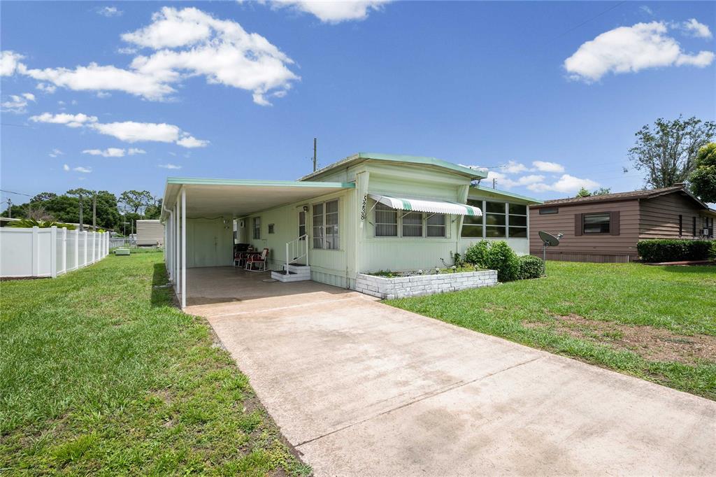 A light green mobile home features a concrete driveway, a carport, and a small garden — 5238 BETMAR DRIVE, ZEPHYRHILLS, FL