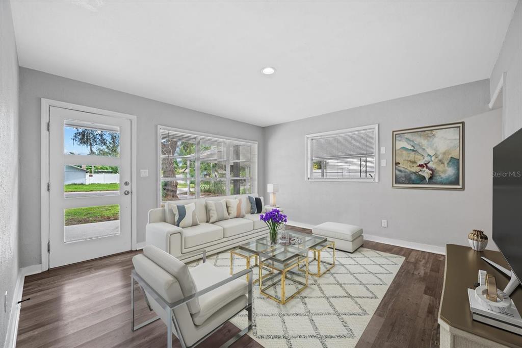 A bright living room features a white sofa, glass coffee tables, and wood-look flooring — 305 E BOUGAINVILLEA AVENUE, TAMPA, FL