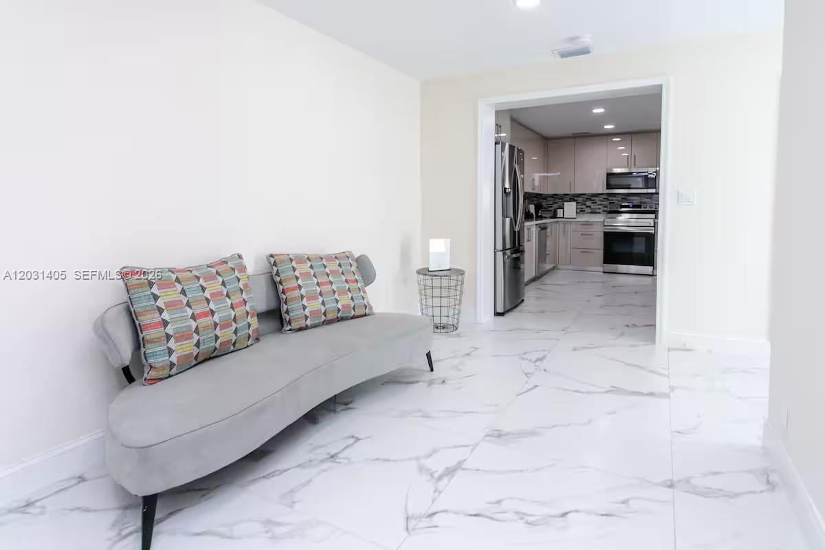 A gray sofa sits on white marble floors in a room adjacent to a kitchen — 1716 Liberty St, Hollywood FL 33020, HOLLYWOOD, FL