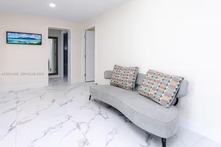 A curved gray sofa sits on white marble-look tile flooring in a minimalist hallway — 1716 Liberty St, Hollywood FL 33020, HOLLYWOOD, FL