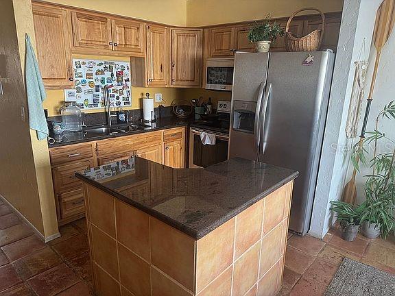 A kitchen features wood cabinets, dark granite countertops, a tiled island, and stainless steel appliances — 525 MANATEE COURT UNIT 8, VENICE, FL