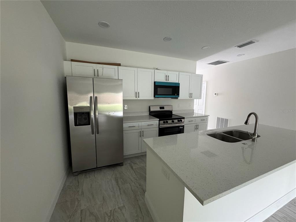A kitchen features white cabinets, stainless steel appliances, and a quartz-topped island with a sink — 310 S 9TH AVENUE, BARTOW, FL