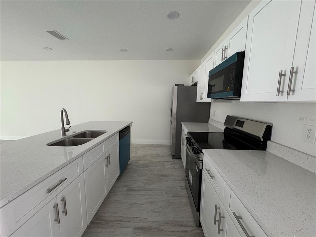 A modern kitchen features white cabinets, quartz countertops, stainless steel appliances, and a central island — 310 S 9TH AVENUE, BARTOW, FL