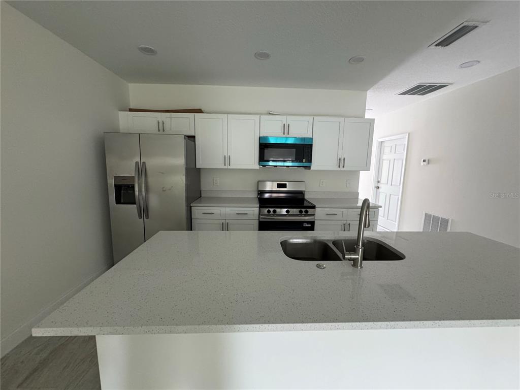 A kitchen features white cabinets, stainless steel appliances, and a large quartz-topped island — 310 S 9TH AVENUE, BARTOW, FL