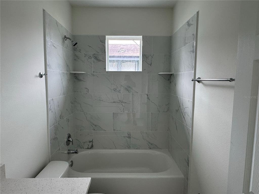 A bathroom features a white bathtub surrounded by marble-look tile walls and a small window — 310 S 9TH AVENUE, BARTOW, FL