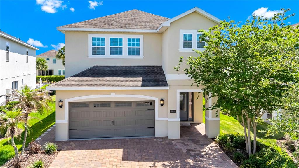 A two-story suburban house features a tan exterior, a gray garage door, and a paver driveway — 7708 GRABEN STREET, KISSIMMEE, FL
