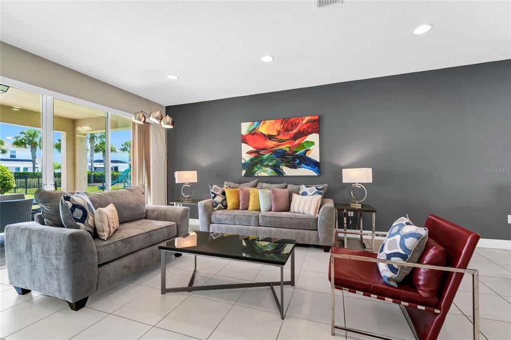 A living room features gray sofas, a red leather chair, and a large abstract painting — 7708 GRABEN STREET, KISSIMMEE, FL
