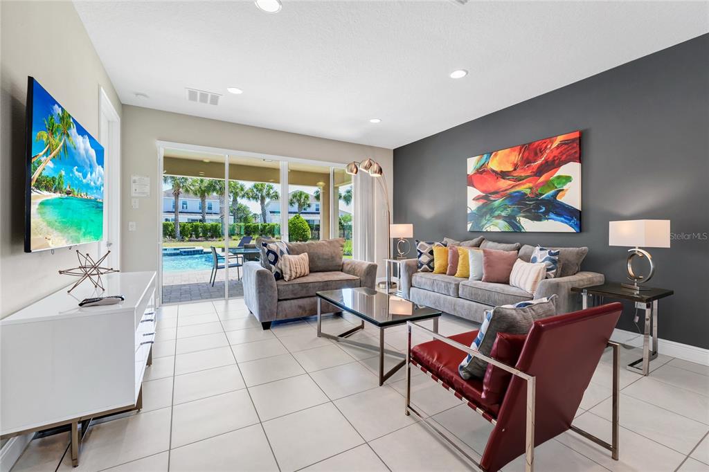 A living room features gray sofas, a red chair, a glass coffee table, and pool views — 7708 GRABEN STREET, KISSIMMEE, FL