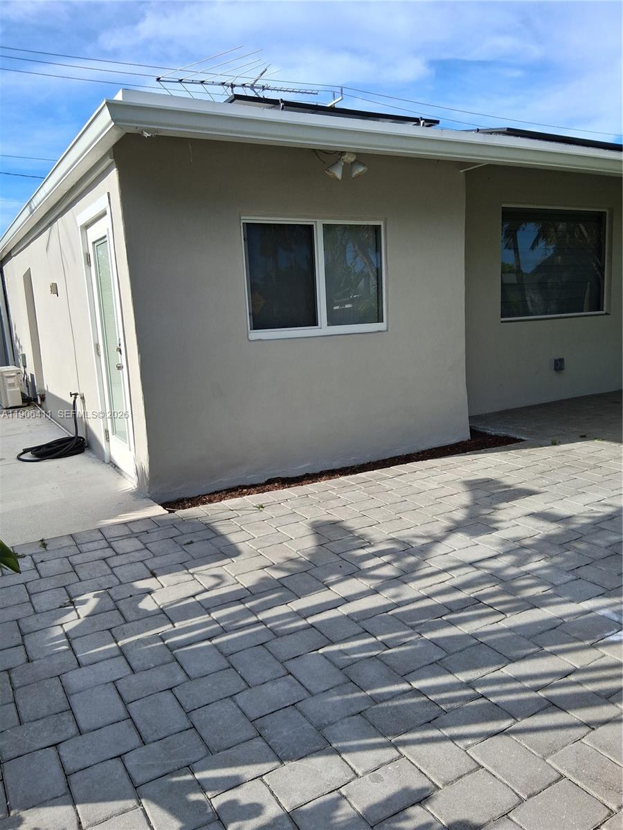 A beige exterior wall features a sliding glass door, a window, and a paved patio — 717 SE 2nd St, Deerfield Beach FL 33441, DEERFIELD BEACH, FL