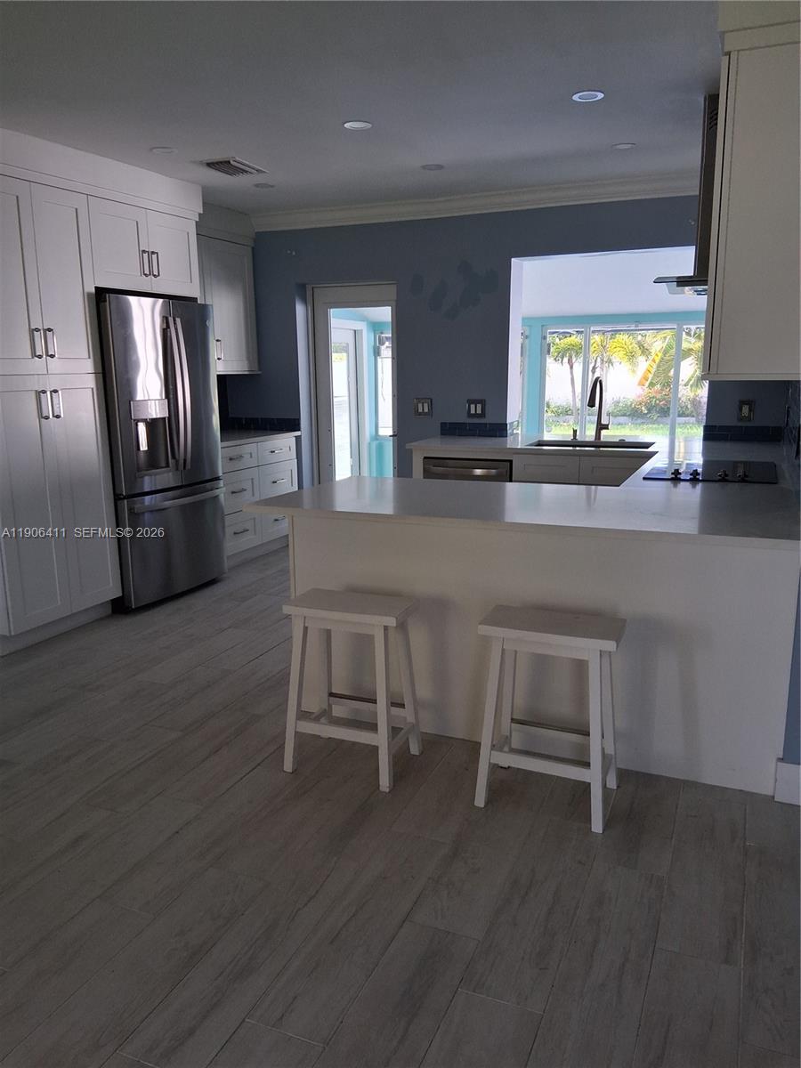 A kitchen features white cabinets, stainless steel appliances, a breakfast bar, and light wood flooring — 717 SE 2nd St, Deerfield Beach FL 33441, DEERFIELD BEACH, FL