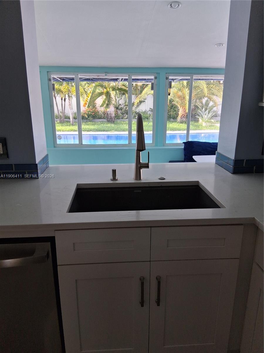 A kitchen sink with a modern faucet overlooks a backyard pool through large windows — 717 SE 2nd St, Deerfield Beach FL 33441, DEERFIELD BEACH, FL