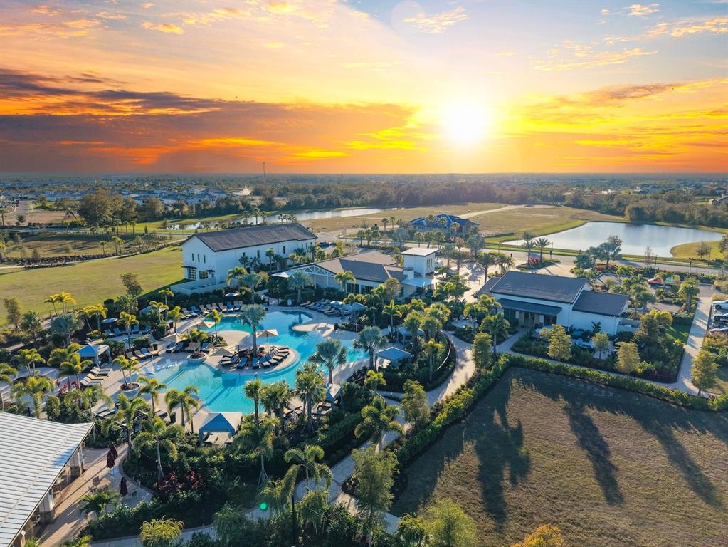 Aerial view of a resort-style swimming pool complex surrounded by palm trees and buildings — 18244 CROPSIDE TRAIL, BRADENTON, FL