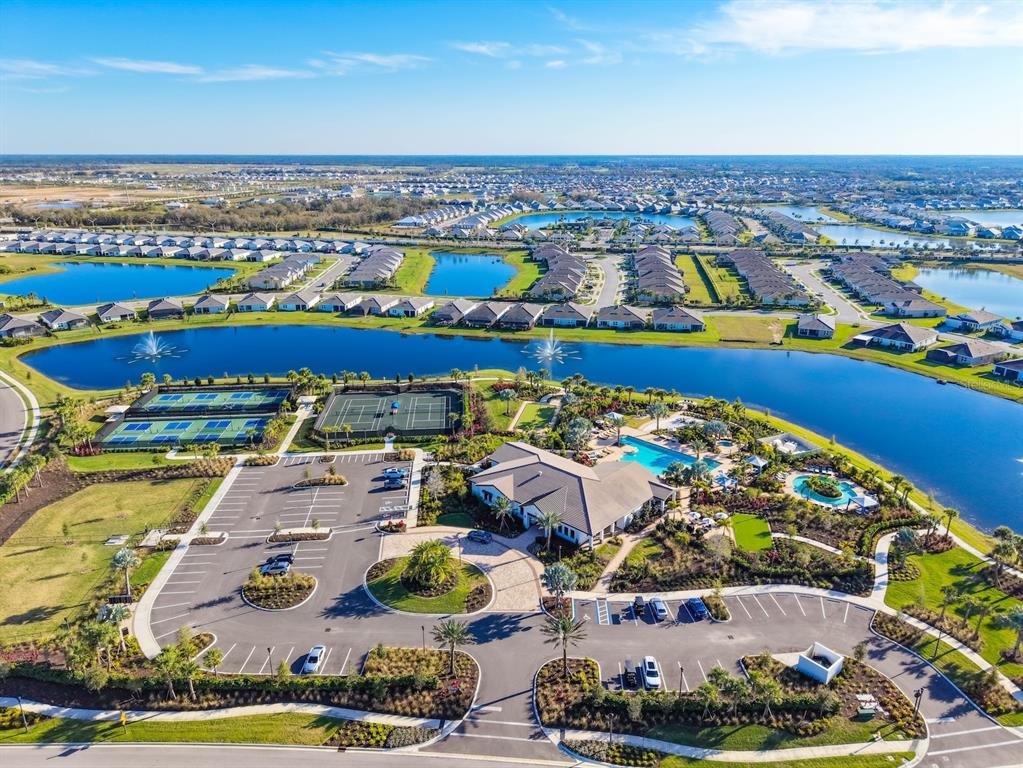 An aerial view shows a community clubhouse with a pool, tennis courts, and surrounding lakes — 18244 CROPSIDE TRAIL, BRADENTON, FL