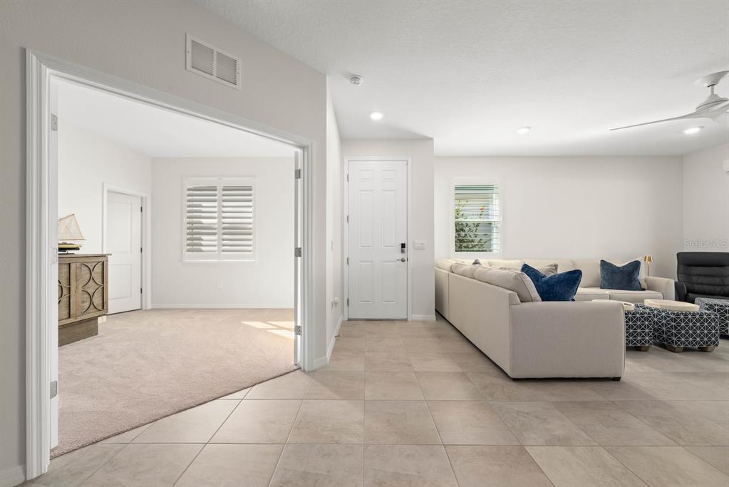 A living room with tile flooring, a beige sofa, and an adjacent carpeted room — 18244 CROPSIDE TRAIL, BRADENTON, FL