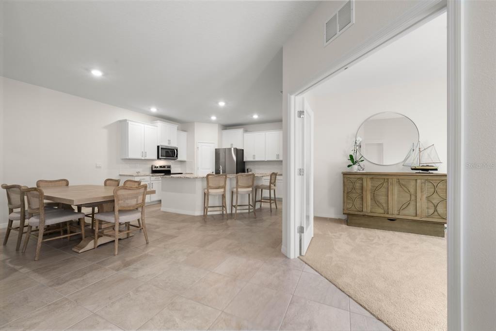 A dining area and kitchen with white cabinets and a breakfast bar open to a room — 18244 CROPSIDE TRAIL, BRADENTON, FL