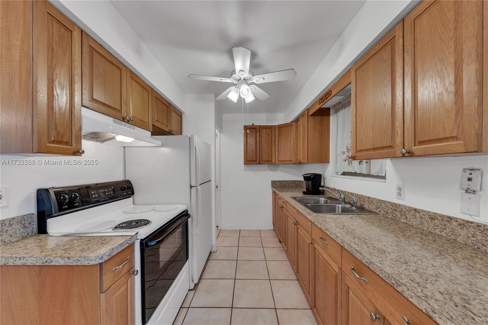 A galley kitchen features oak cabinets, laminate countertops, white appliances, and light-colored floor tiles — 2300 Jackson St # 10, Hollywood FL 33020, HOLLYWOOD, FL