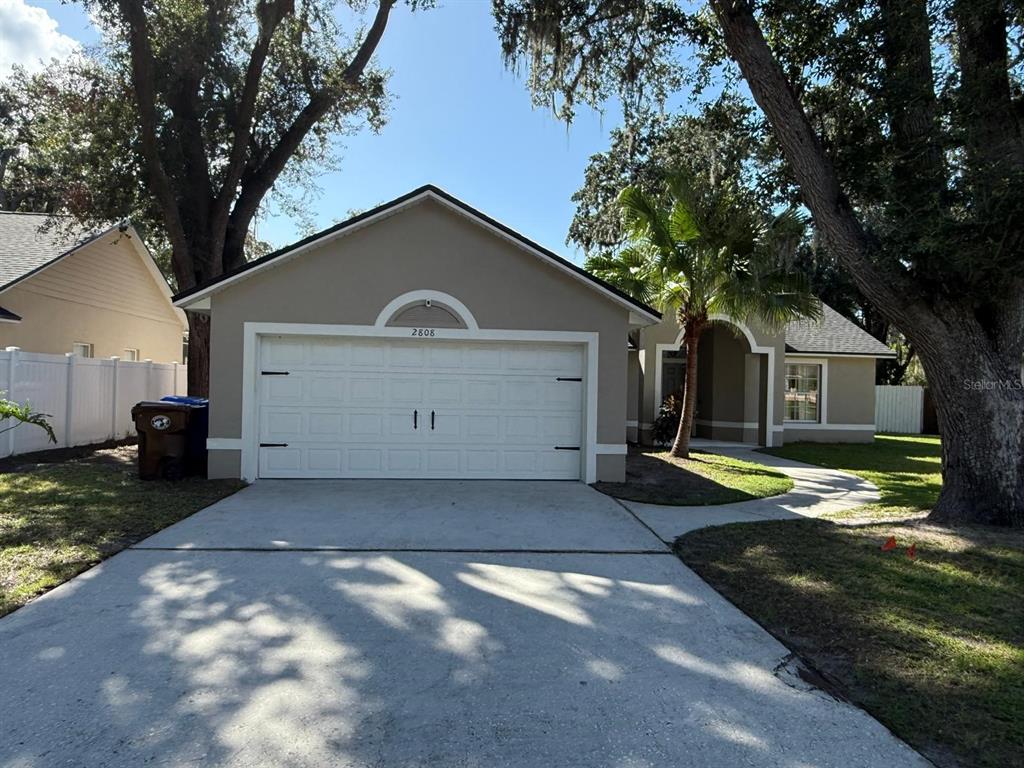 A beige single-story house features a white two-car garage, a palm tree, and a walkway — 2808 MILL RUN BOULEVARD, KISSIMMEE, FL
