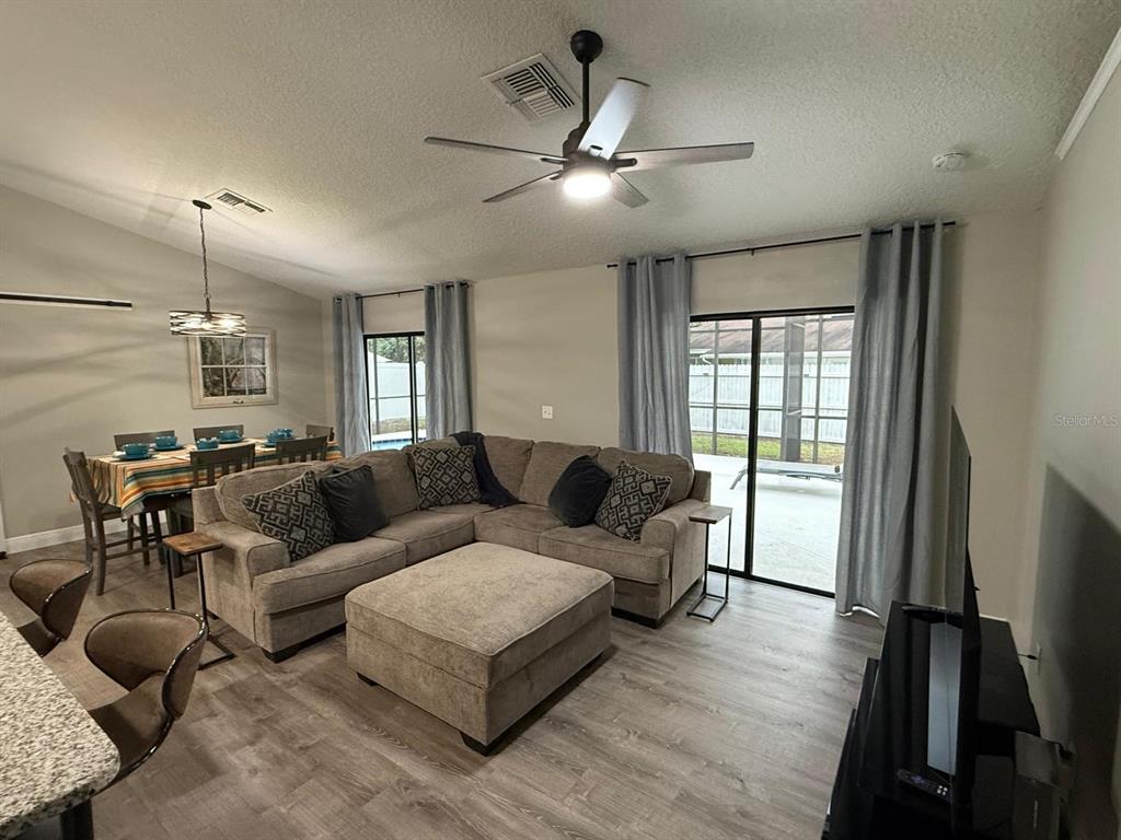 An open-concept living and dining area features a sectional sofa, wood-look flooring, and sliding doors — 2808 MILL RUN BOULEVARD, KISSIMMEE, FL