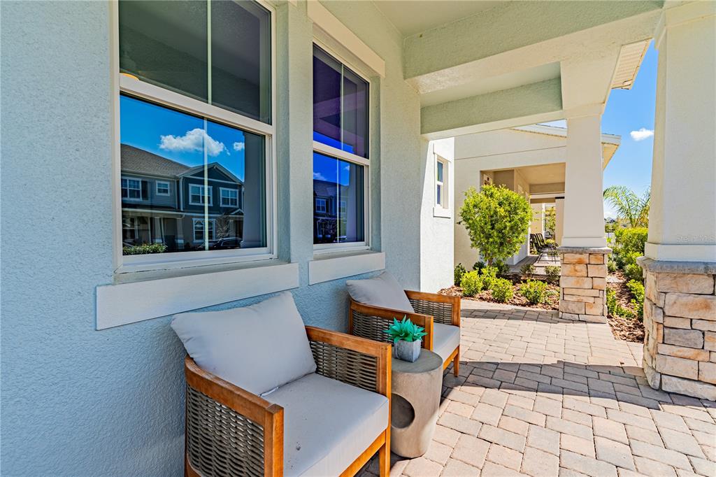 A covered front porch features two chairs, a small table, and stone pillar accents — 15197 BLUE PEACOCK LANE, WINTER GARDEN, FL