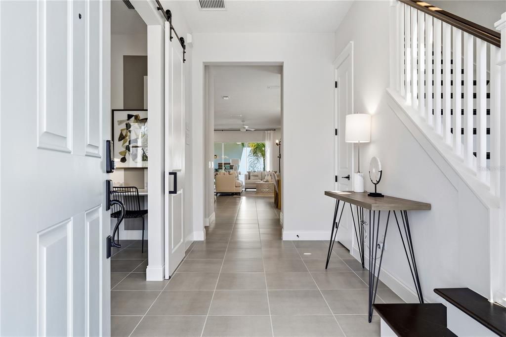 A bright entryway features tile flooring, a staircase with white railings, and a sliding barn door — 15197 BLUE PEACOCK LANE, WINTER GARDEN, FL
