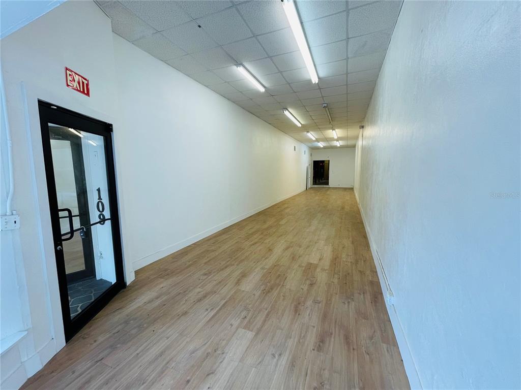 An empty, narrow commercial space features white walls, wood-look flooring, and a drop ceiling — 109 BROADWAY, KISSIMMEE, FL