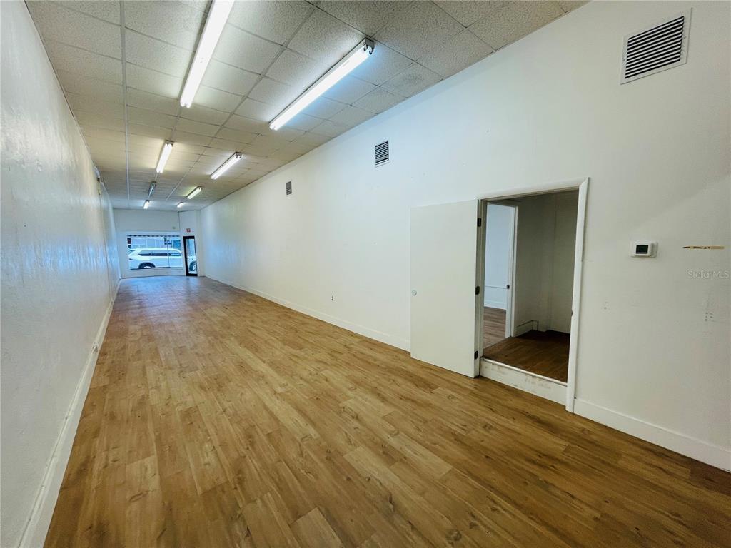 An empty commercial space features wood-look flooring, white walls, and a drop ceiling with lights — 109 BROADWAY, KISSIMMEE, FL