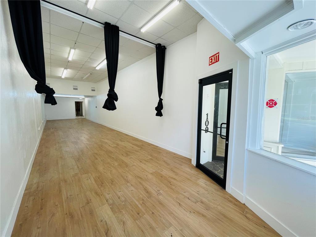 An empty commercial space features light wood-look flooring, white walls, and black curtains — 109 BROADWAY, KISSIMMEE, FL