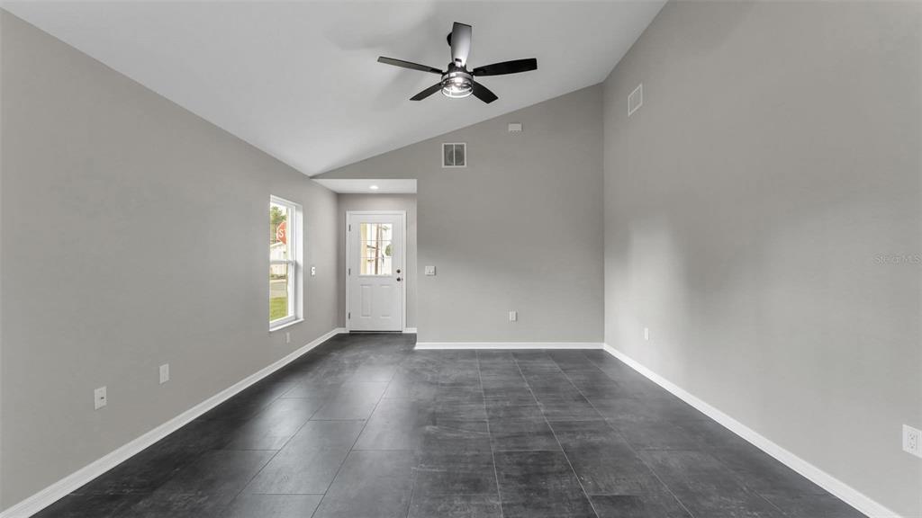 An empty room with gray walls, dark tile flooring, and a vaulted ceiling with a fan — 0 38TH STREET NW, WINTER HAVEN, FL