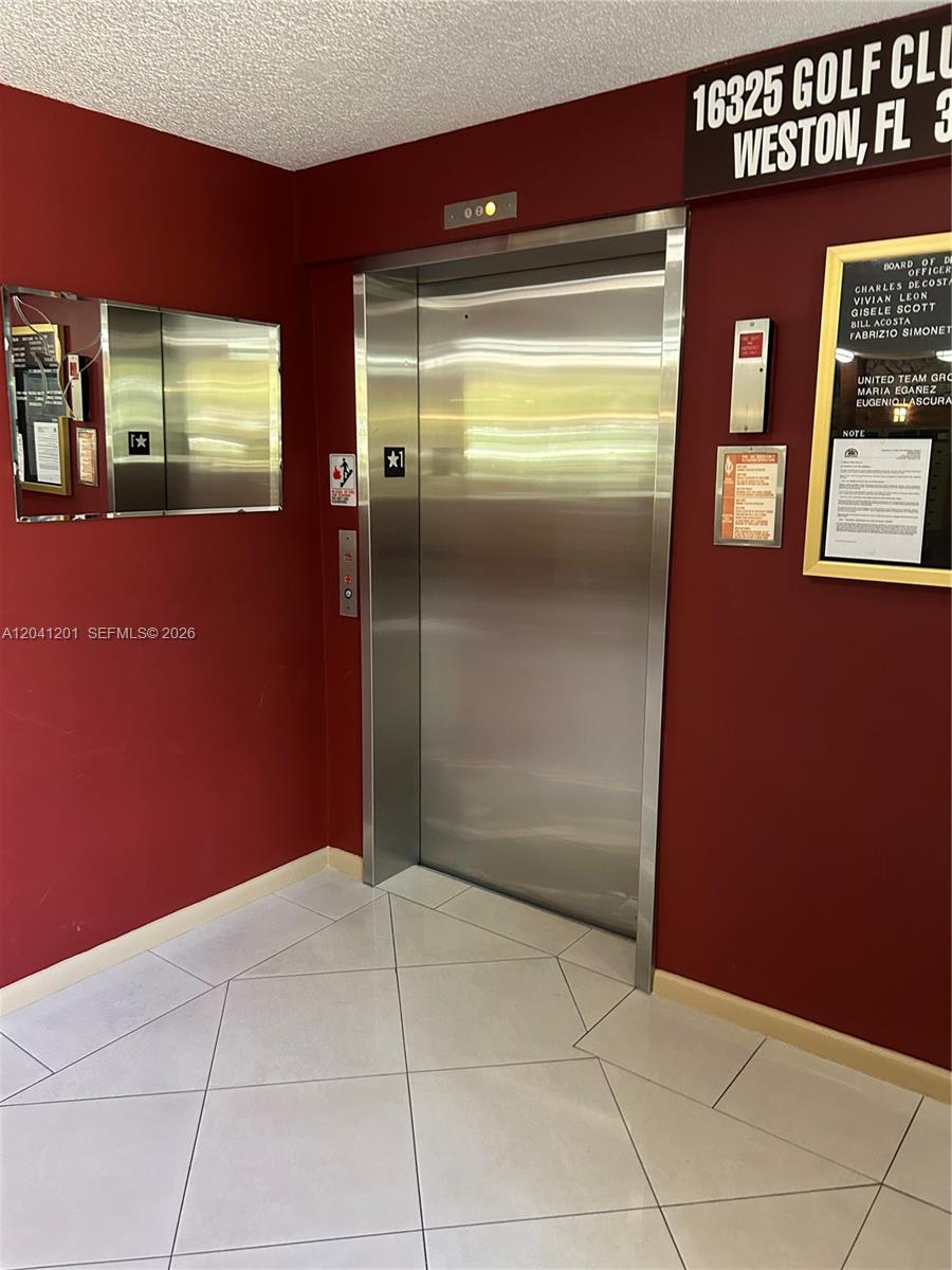A stainless steel elevator door is centered on a red wall in a tiled lobby — 16325 Golf Club Rd # 304, Weston FL 33326, WESTON, FL