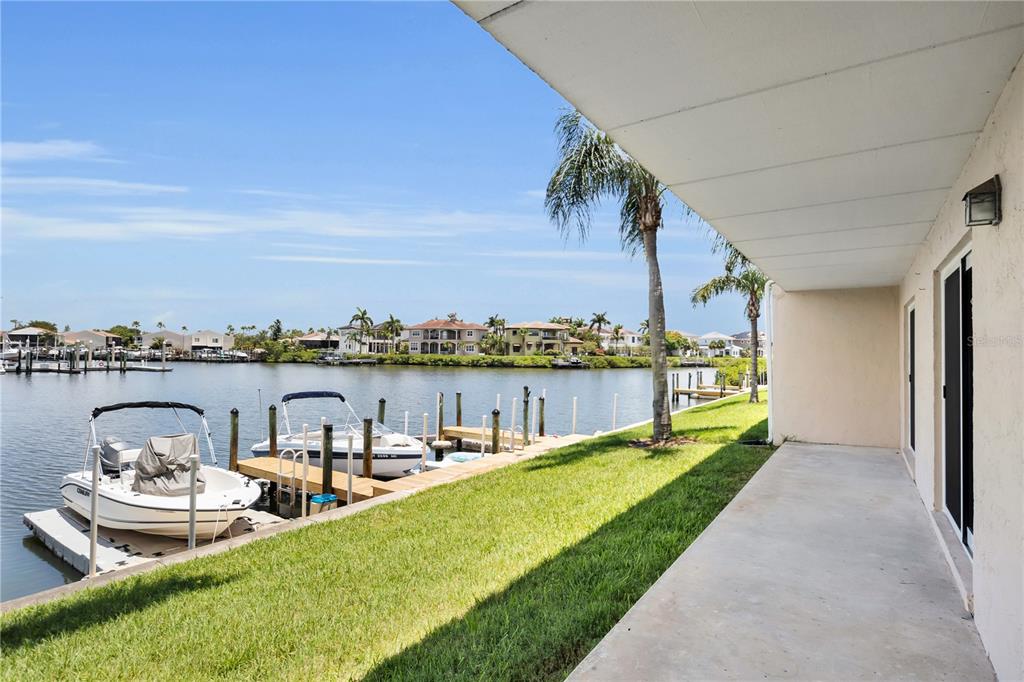 A concrete patio overlooks a grassy lawn, a boat dock, and a canal with houses — 8820 BAY POINTE DRIVE UNIT 102, TAMPA, FL