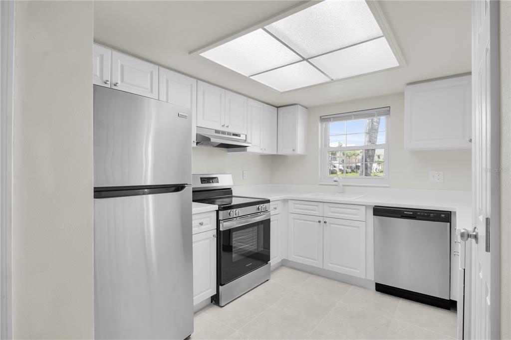 A kitchen features white cabinetry, stainless steel appliances, and a window above the sink — 8820 BAY POINTE DRIVE UNIT 102, TAMPA, FL