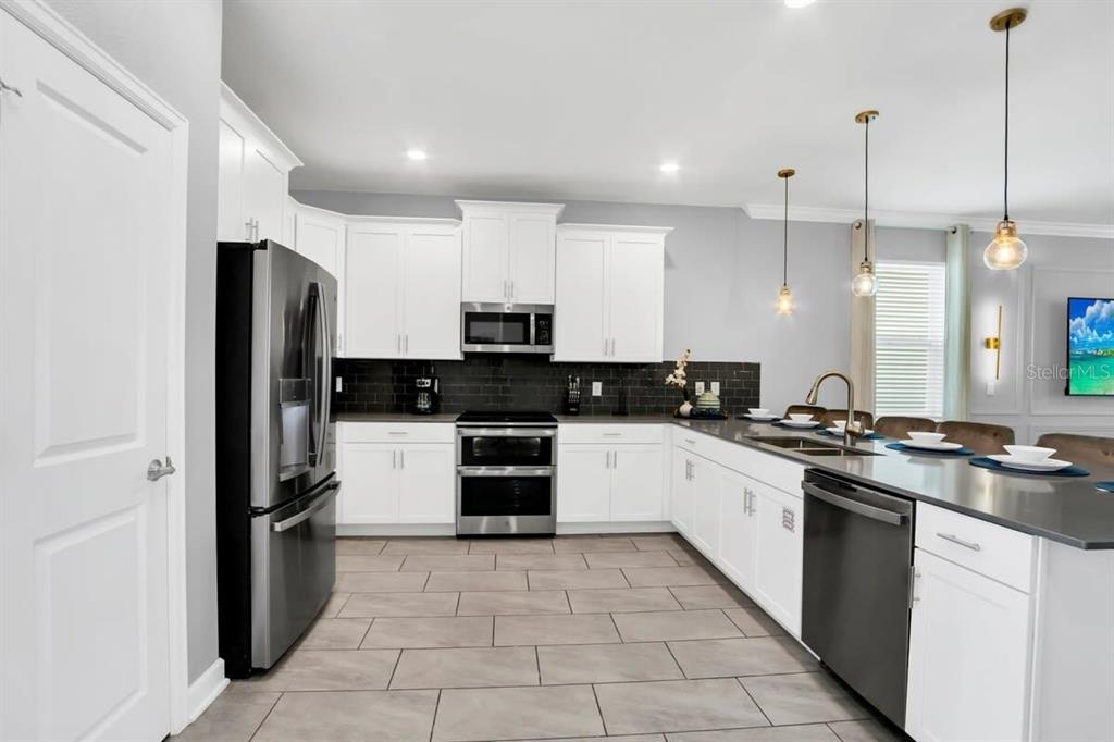 A modern kitchen features white cabinets, stainless steel appliances, a dark tile backsplash, and tile flooring — 4388 QUOTE STREET, KISSIMMEE, FL
