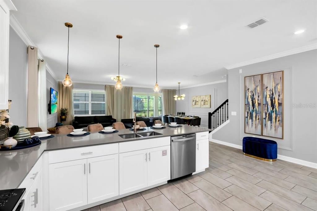 A modern kitchen with white cabinets, gray countertops, and pendant lighting overlooks an open living area — 4388 QUOTE STREET, KISSIMMEE, FL