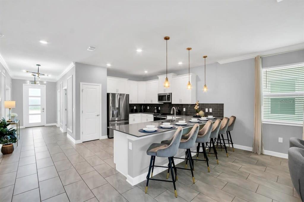 A modern kitchen features white cabinetry, a gray island with bar seating, and tile flooring — 4388 QUOTE STREET, KISSIMMEE, FL