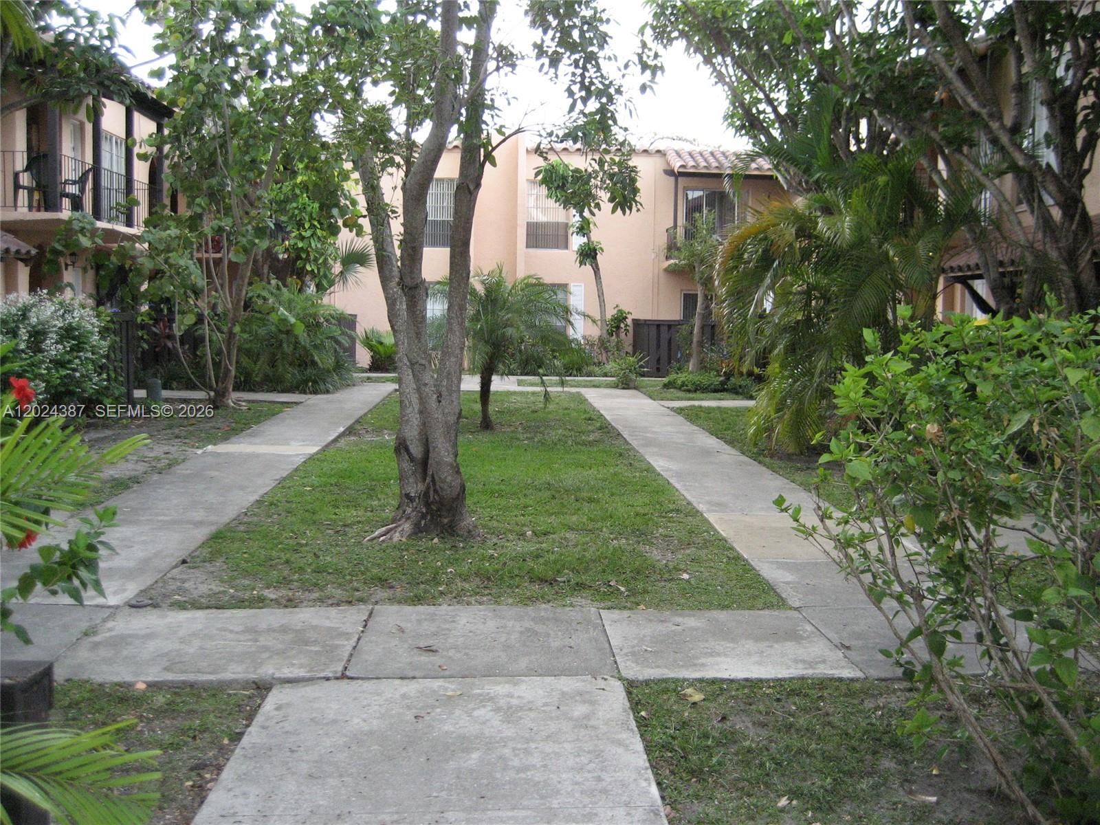 A courtyard with a central lawn, concrete walkways, and surrounding apartment buildings with trees — 10806 N Kendall Dr # 26, Miami FL 33176, MIAMI, FL