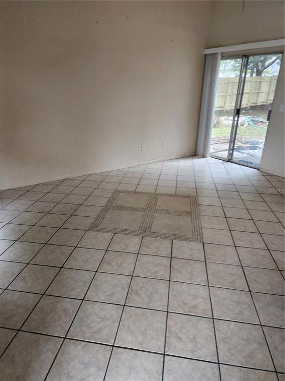 An empty room features beige tile flooring with a decorative mosaic inlay and sliding glass doors — 2747 KAVALIER DRIVE, PALM HARBOR, FL