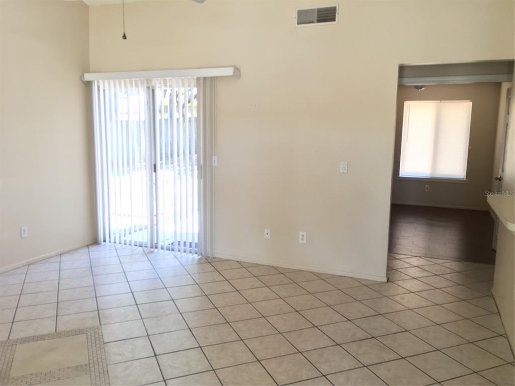 An empty room with beige tile flooring, a sliding glass door, and an adjacent room — 2747 KAVALIER DRIVE, PALM HARBOR, FL