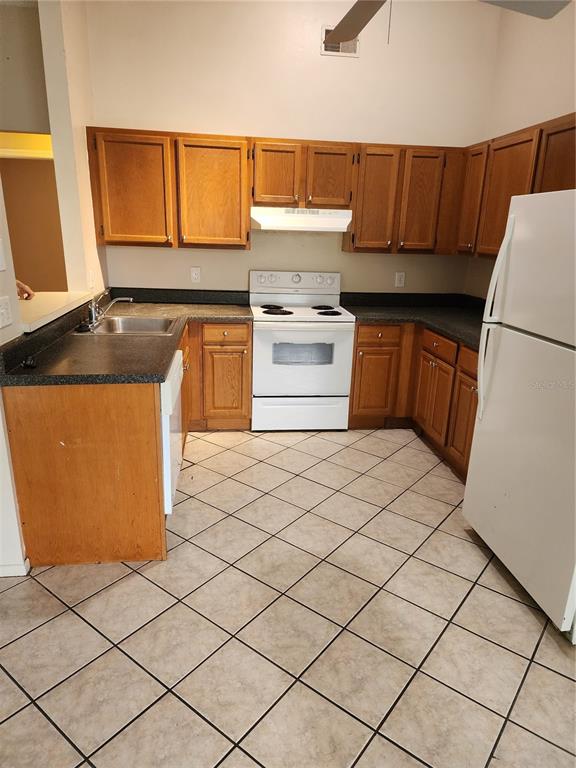 A kitchen features wood cabinets, white appliances, dark countertops, and light-colored tile flooring — 2747 KAVALIER DRIVE, PALM HARBOR, FL
