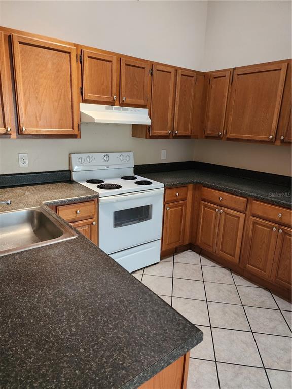 A kitchen features wood cabinets, dark laminate countertops, a white stove, and tiled flooring — 2747 KAVALIER DRIVE, PALM HARBOR, FL