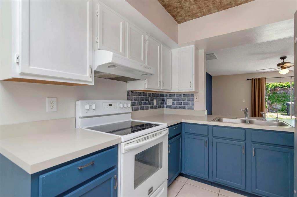 A kitchen features white upper cabinets, blue lower cabinets, a white stove, and tile backsplash — 14053 NOTREVILLE WAY, TAMPA, FL