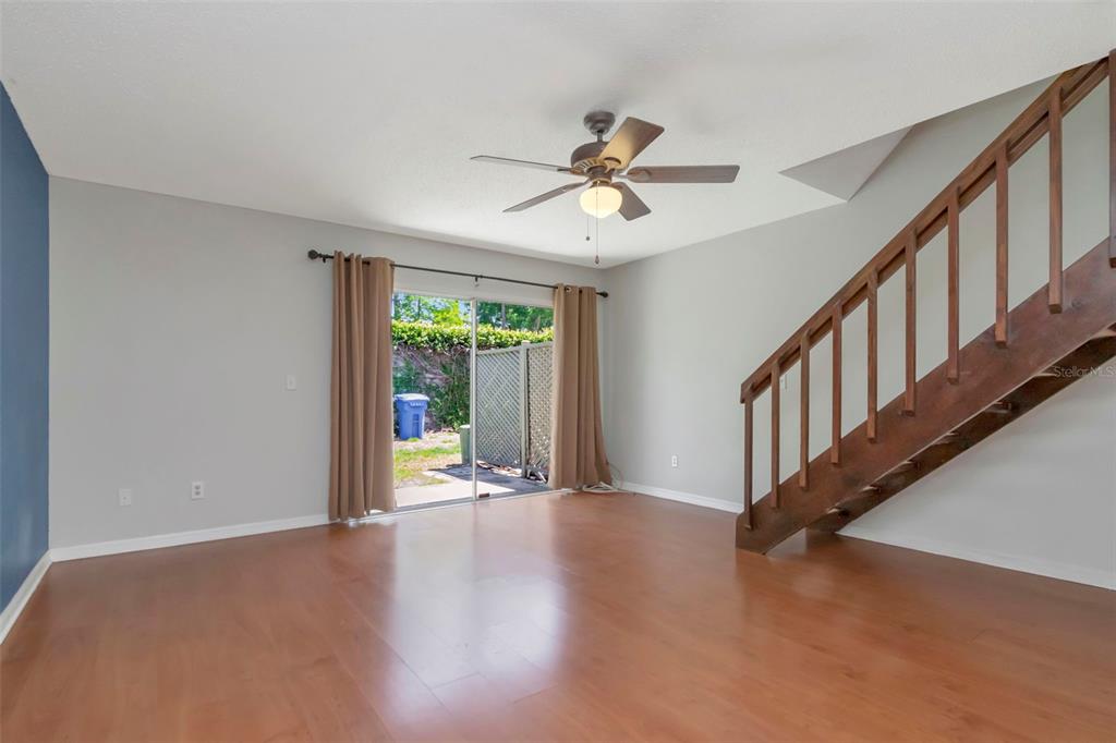 A living room with wood flooring, a wooden staircase, and a sliding glass door — 14053 NOTREVILLE WAY, TAMPA, FL