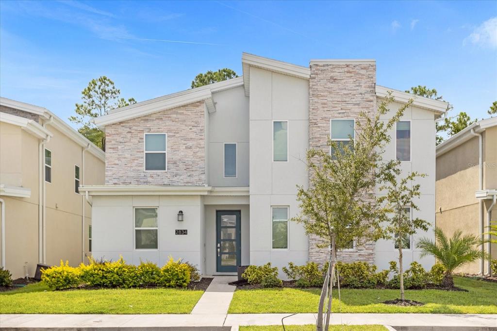 A two-story modern house features a stone facade, white siding, and a blue front door — 2834 STOREY COVE AVENUE, KISSIMMEE, FL