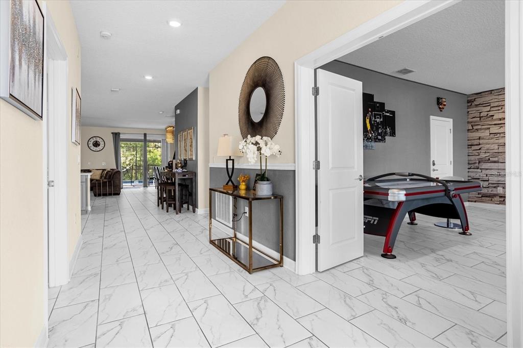 A hallway with white marble-look tile flooring leads to a living area and game room — 2834 STOREY COVE AVENUE, KISSIMMEE, FL