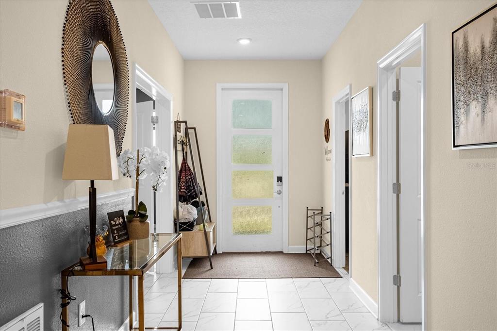 A bright entryway features white tile floors, a glass-topped console table, and a front door — 2834 STOREY COVE AVENUE, KISSIMMEE, FL