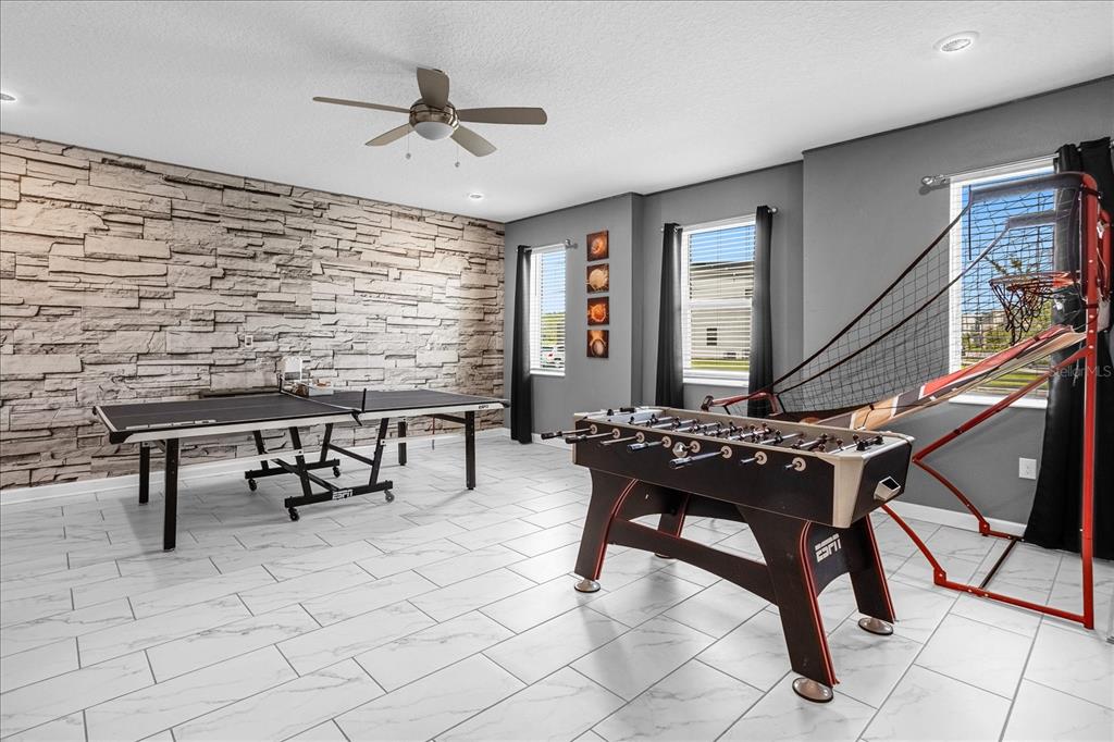 A game room features a stone accent wall, tile flooring, a ping pong table, and foosball — 2834 STOREY COVE AVENUE, KISSIMMEE, FL
