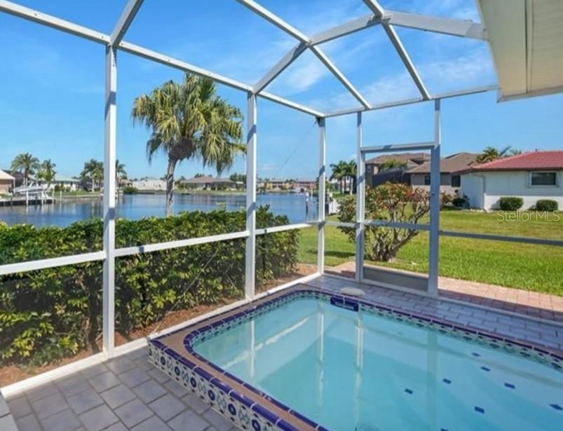 A screened-in patio features a small tiled pool overlooking a canal and neighboring houses — 3433 NIGHTHAWK COURT, PUNTA GORDA, FL