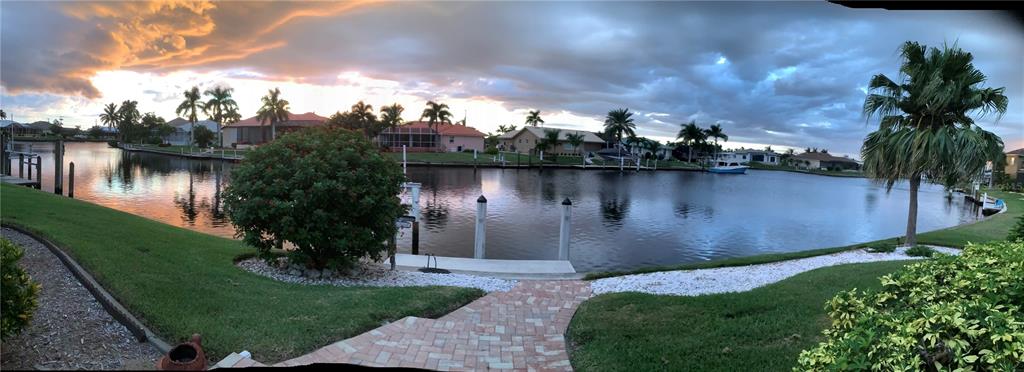 A panoramic view of a canal-front backyard with a brick walkway, lawn, and palm trees — 3433 NIGHTHAWK COURT, PUNTA GORDA, FL